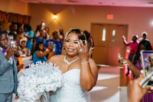 Happy bride in white dress holding crystal bouquet waves joyfully at wedding reception celebration.