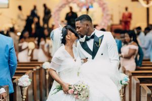 Newlyweds share romantic moment in church with floral arch in background.