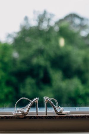 Silver wedding heels positioned on a ledge with blurred green foliage in the background.