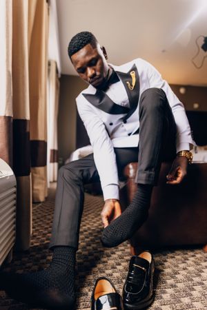 Groom in white tuxedo and bow tie adjusting his dress shoes.
