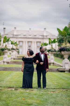 A couple stands on a formal garden path with a stately white building in the distance.