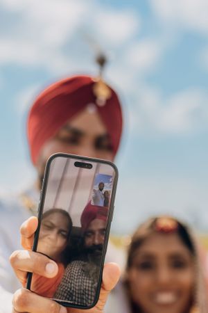 A close-up shot of a phone screen showing a wedding selfie being taken.
