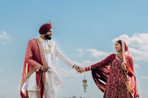 A couple in red and white traditional wedding attire holds hands against a blue sky.