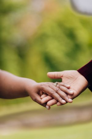 Close up of hands with engagement ring being exchanged against blurred green background.