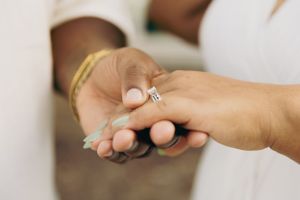 Close-up of hands holding engagement ring with white manicured nails.