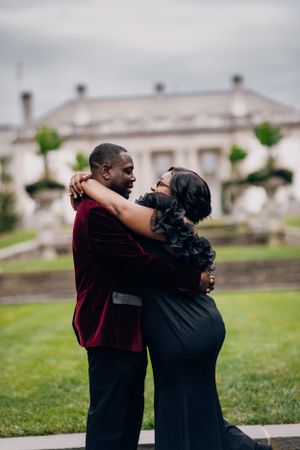 Romantic couple sharing intimate embrace on mansion grounds during formal photoshoot.