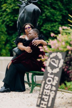 Couple sits together on green park bench with decorative statue in background.