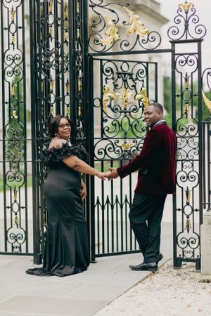 A couple in formal attire poses by an ornate wrought iron gate entrance.
