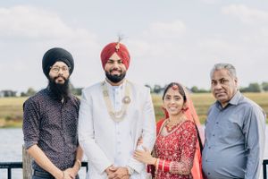 A wedding party poses together outdoors wearing traditional Sikh and Indian formal attire.