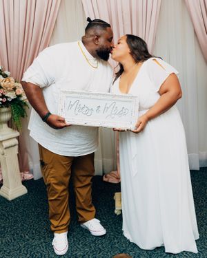 Couple holding 'Mr & Mrs' sign while sharing intimate moment in wedding attire.