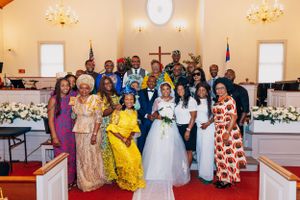 Large wedding party group photo in a church with colorful traditional attire and decorative flowers.