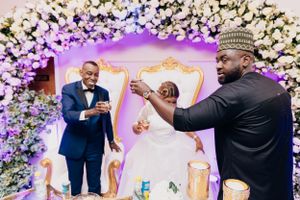 Celebratory moment at wedding reception with floral arch backdrop and decorative throne chairs.