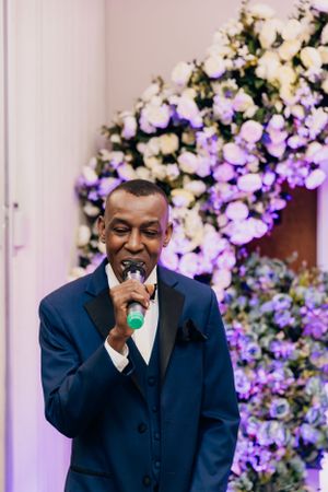 Speaker performing with microphone against a beautiful purple and white flower wall display.