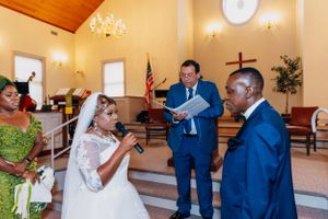 A wedding ceremony takes place inside a church with decorative lighting and an American flag.