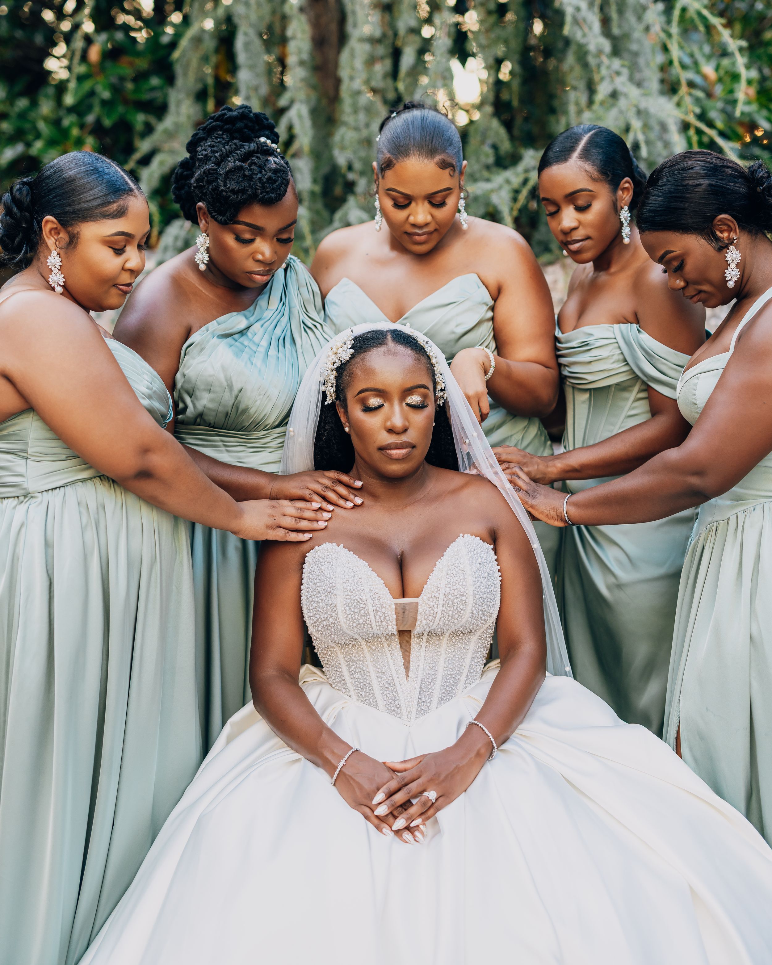 Wedding party in sage green bridesmaid dresses posing together with a bride in a white gown.