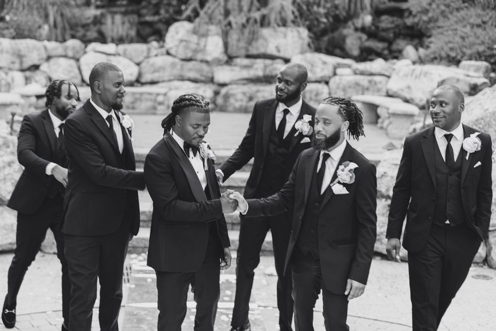 Groomsmen in black tuxedos pose together for formal wedding photos.