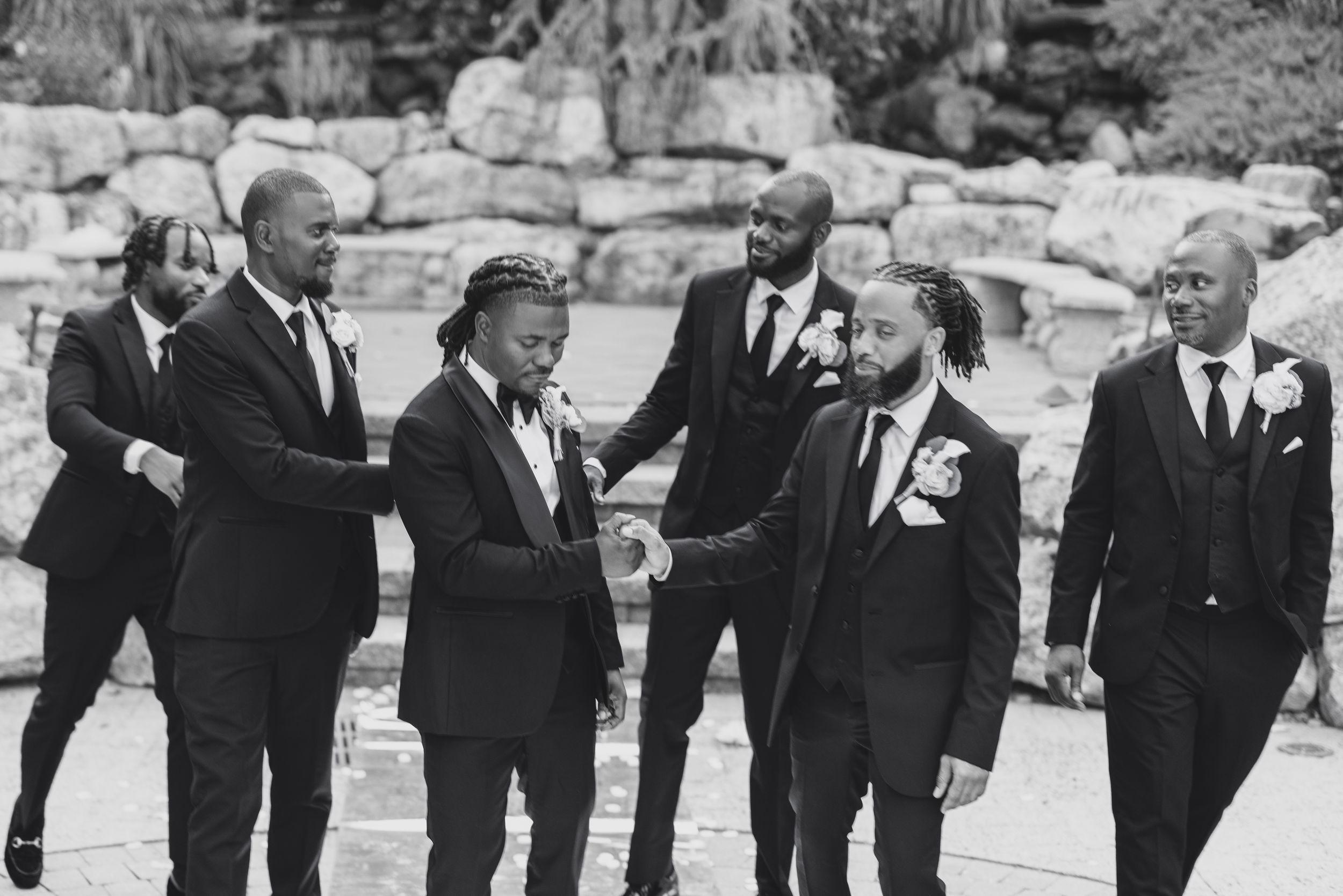 Groomsmen in black tuxedos pose together for formal wedding photos.
