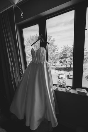 White wedding dress hanging in natural window light creating a dramatic silhouette.