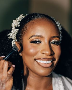 Close-up shots of a bride getting her makeup professionally done while wearing a pearl hair accessory and white robe.