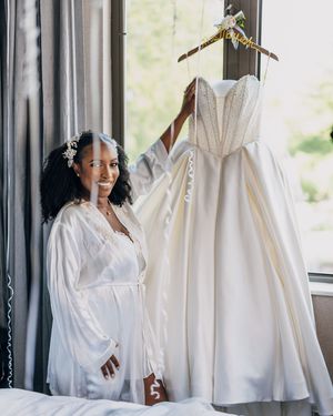 Wedding party preparations with white robes and gowns against a bright window backdrop.