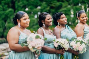 Bridesmaids dressed in soft sage green dresses holding white bouquets outdoors.