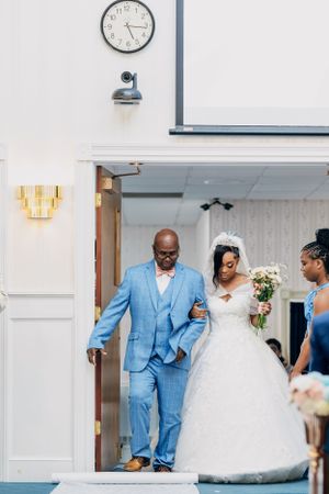 A wedding couple walks down church steps with the bride in white and a gentleman in a light blue suit.