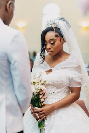 Bride holding simple bouquet looks down during intimate wedding ceremony moment.