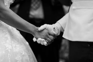 A black and white close-up of two people holding hands during a wedding ceremony.