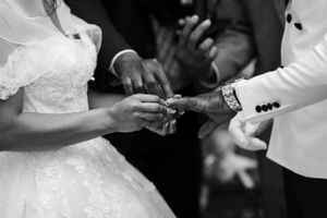 A close-up black and white shot of hands exchanging wedding rings during a ceremony.