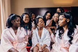 Group of bridesmaids in pink robes share joyful moment with bride during wedding preparations.