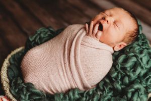 Sleeping newborn wrapped in soft pink swaddle against textured backdrop. Annapolis newborn photographer