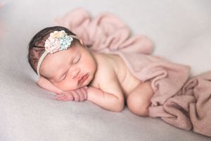 Peaceful newborn baby sleeping on pink blanket wearing delicate floral headband. Annapolis newborn photographer