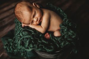 Newborn baby sleeping peacefully on dark green textured blanket. Maryland newborn photographer