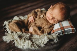 Sleeping newborn wrapped in cozy brown blanket on cream textured surface. Annapolis Newborn photographer