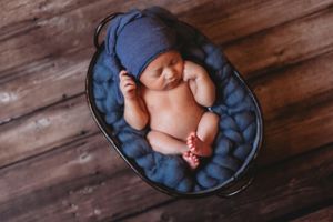 Peaceful newborn portrait on blue fabric against dark wooden background. Annapolis newborn photographer