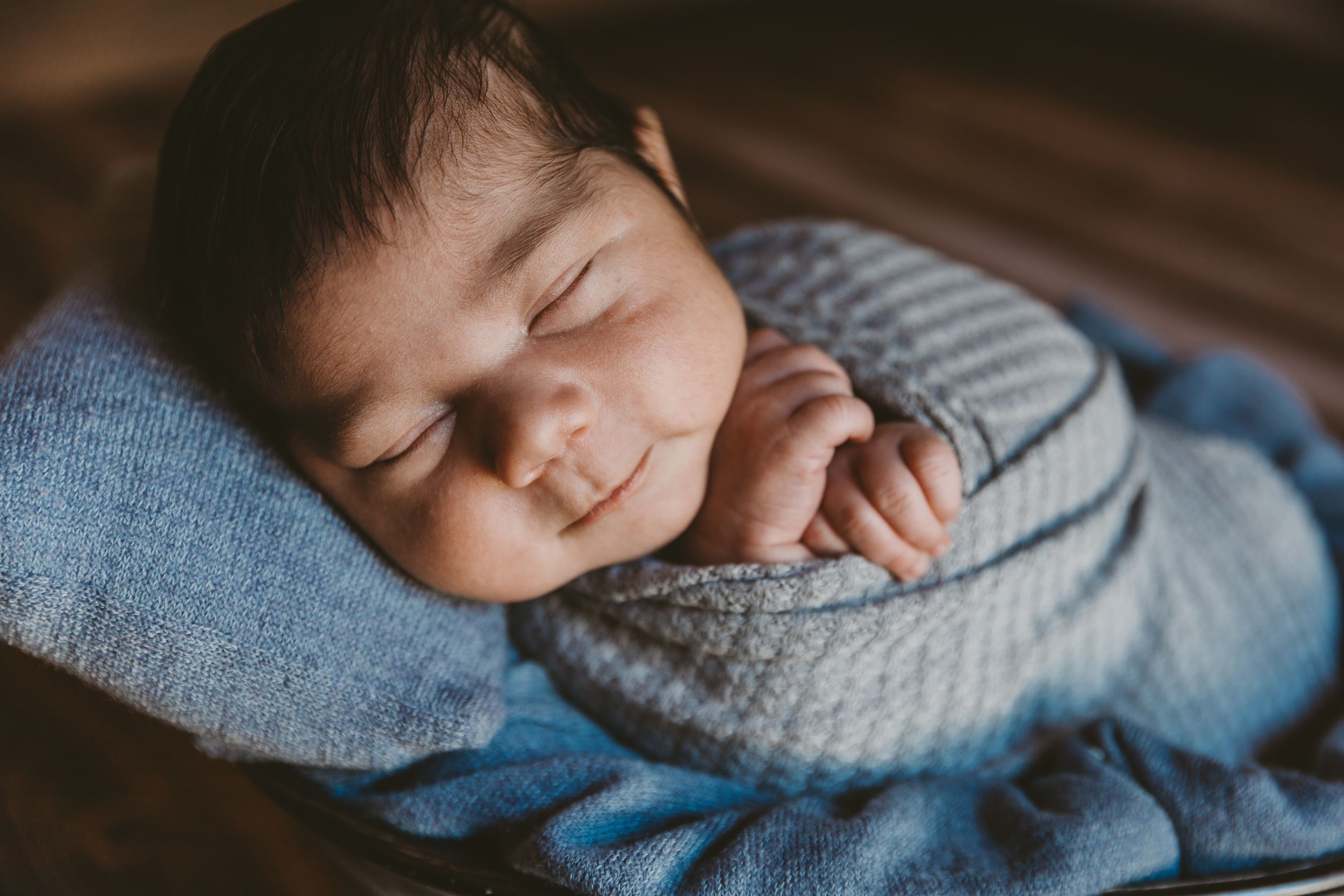 Peaceful newborn baby smiling while swaddled in a soft blue blanket, resting on a cozy pillow.