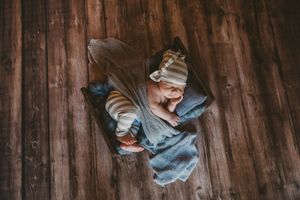Newborn baby sleeping peacefully in a rustic wooden box with soft blankets and a striped hat.