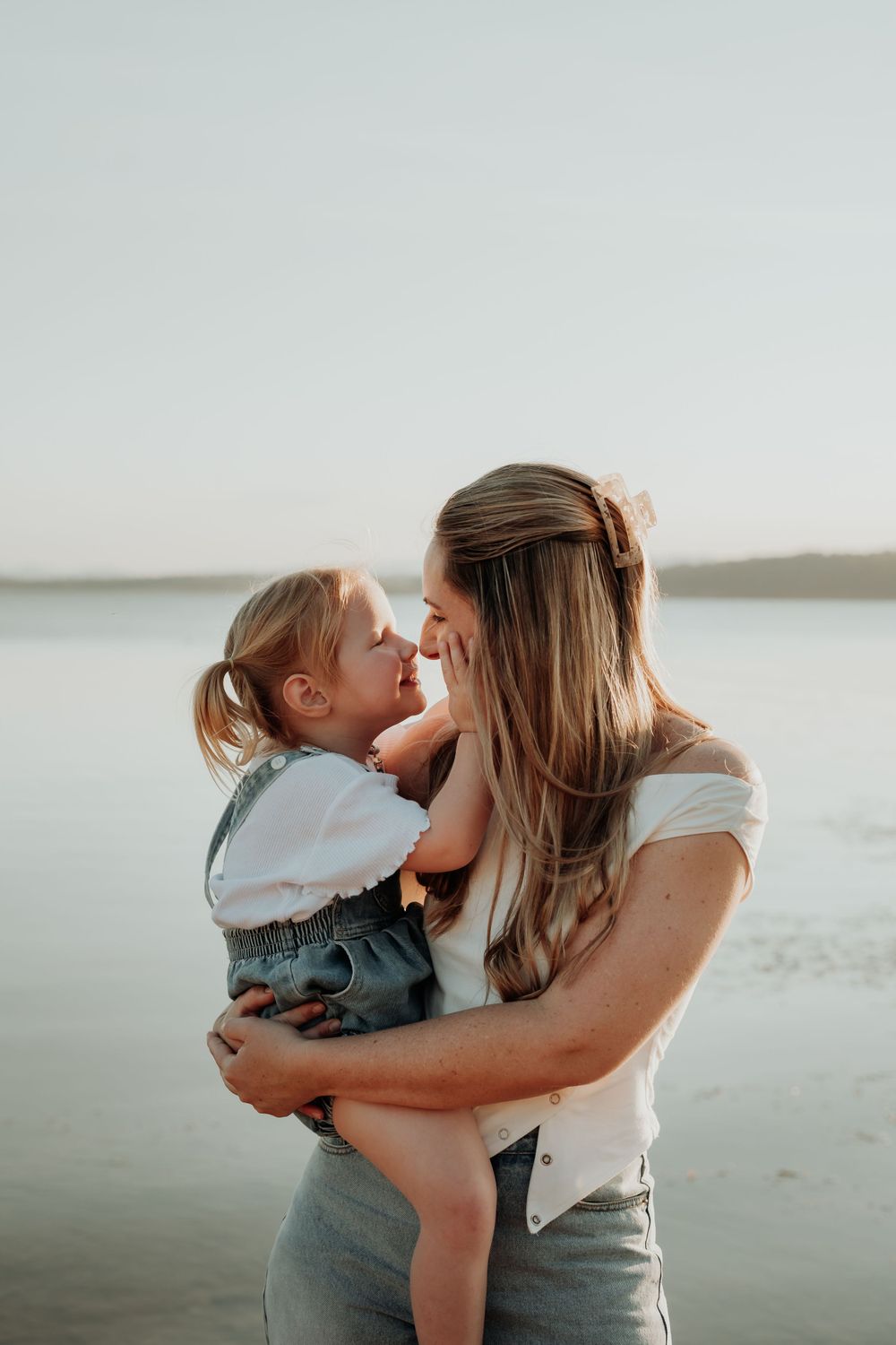 A tender moment between parent and child against a serene waterfront backdrop at sunset.