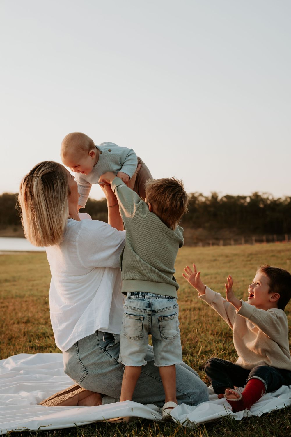 A family sharing a playful moment on a picnic blanket during golden hour at awoonga dam.