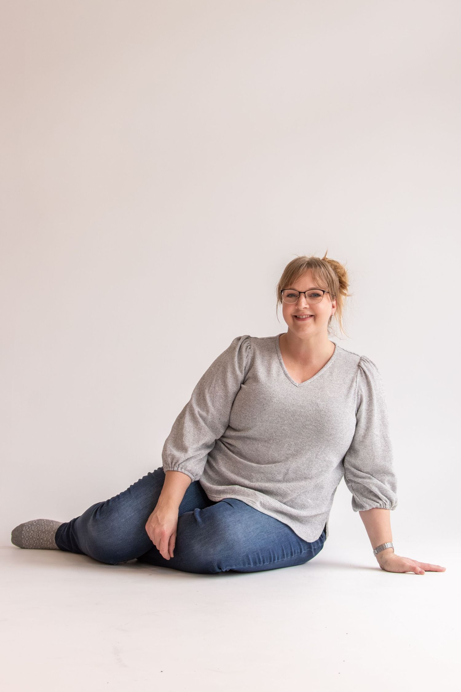 A person in a gray sweater and jeans poses on a white background in a series of relaxed positions.