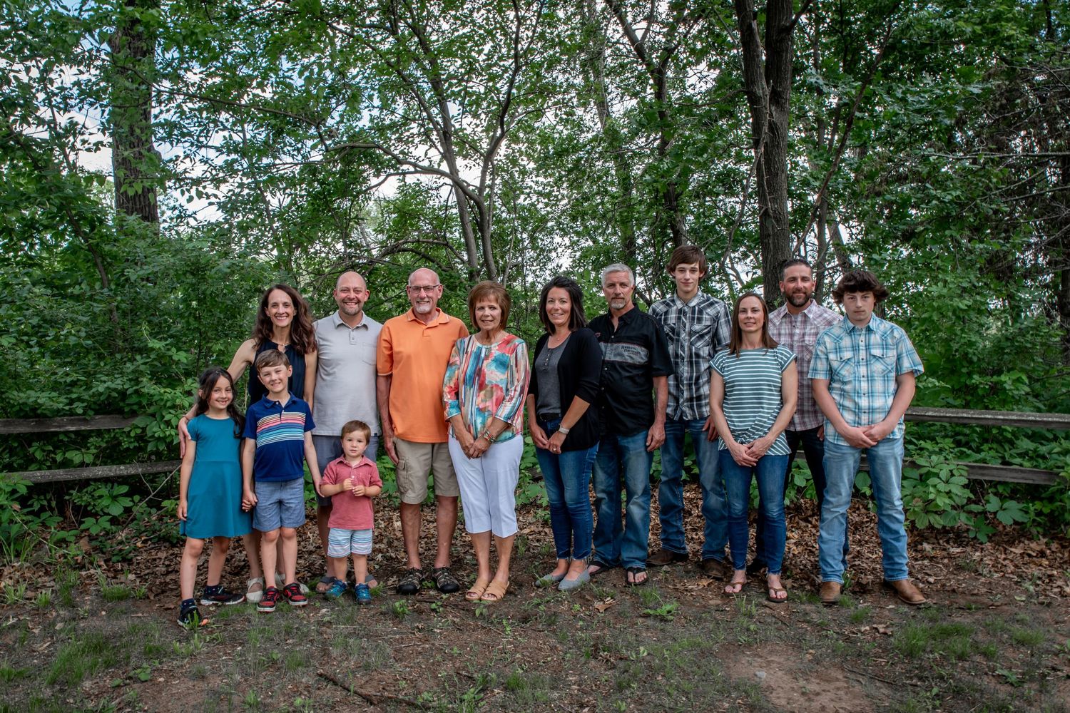 Group photo of family members standing together on wooden deck in lush green setting.