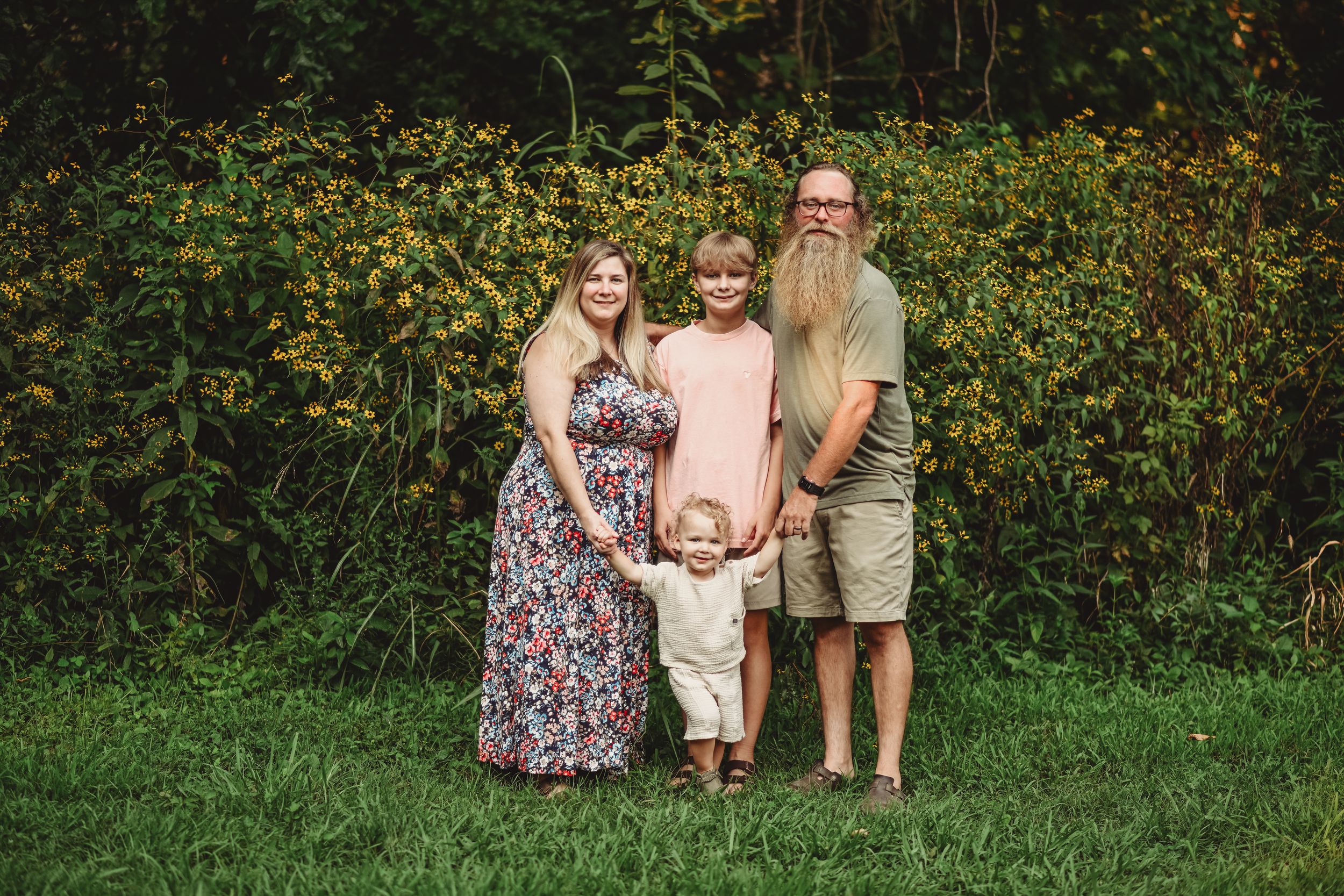 A family of four poses together against a backdrop of wildflowers and greenery.