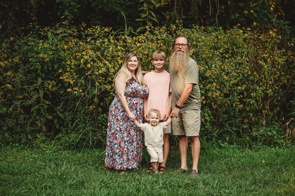 A family of four poses together against a backdrop of wildflowers and greenery.