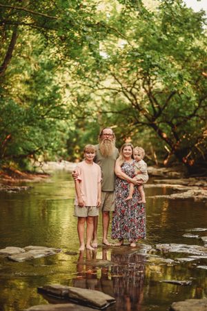 A family stands together on rocks in a serene creek surrounded by lush green trees.