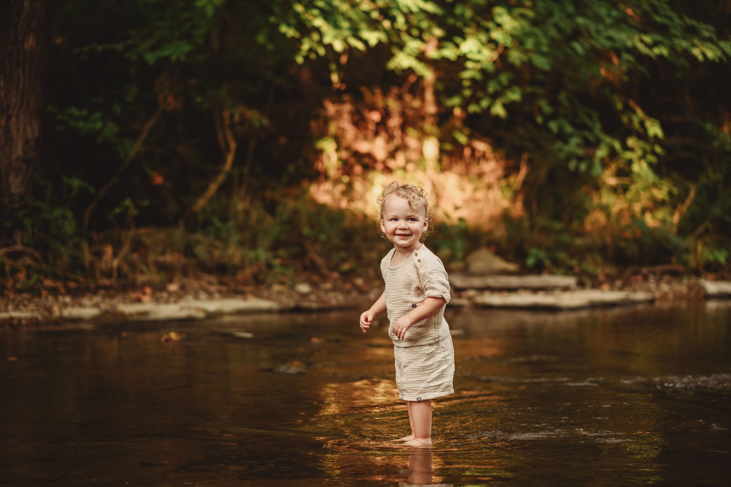 A small child plays in shallow creek water during a sunny afternoon.