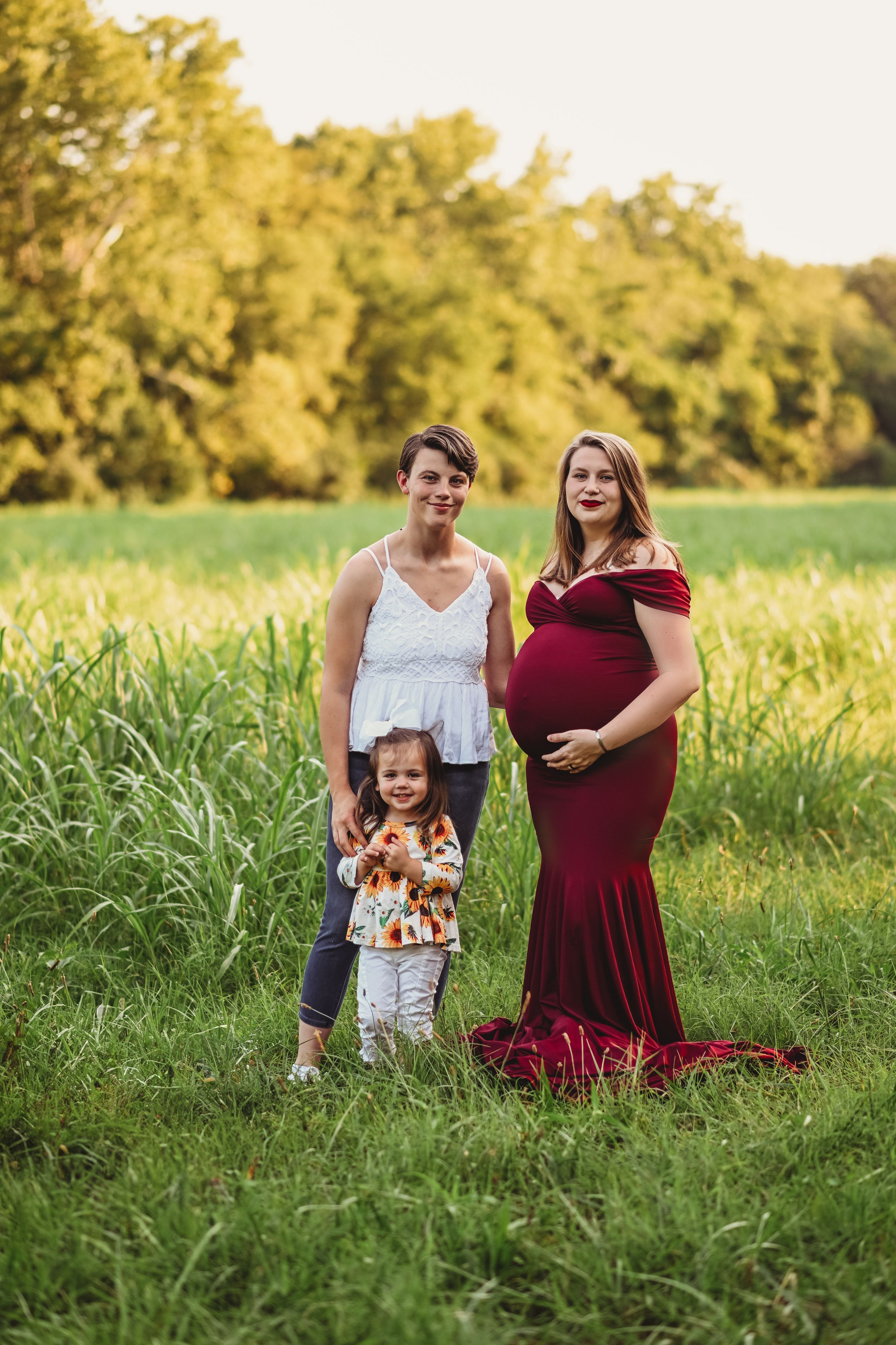 Three people pose together in a golden field during sunset.