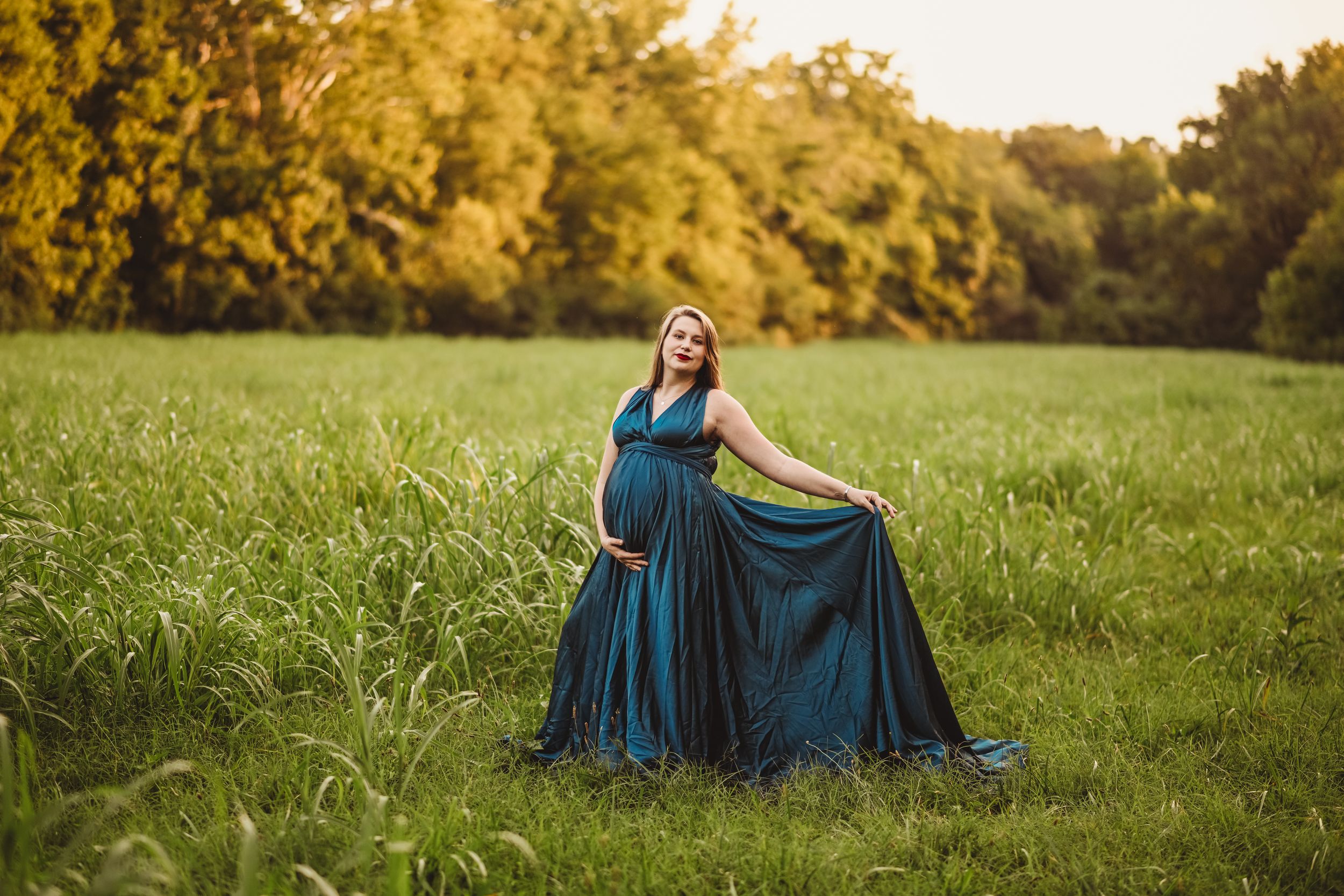 A flowing teal dress catches the golden sunlight in an open meadow during sunset.