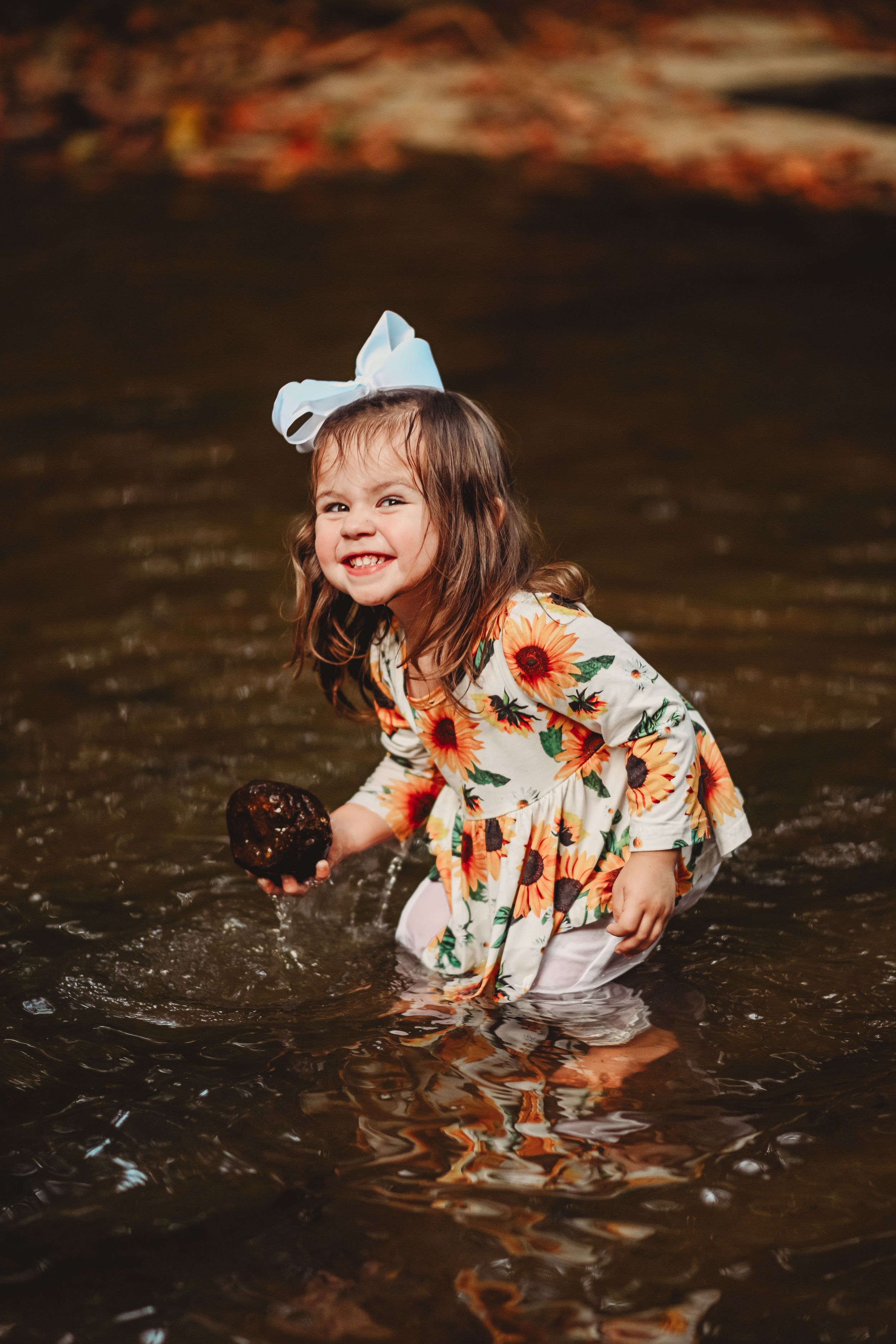 A floral dress splashes in shallow water during a playful outdoor photoshoot.