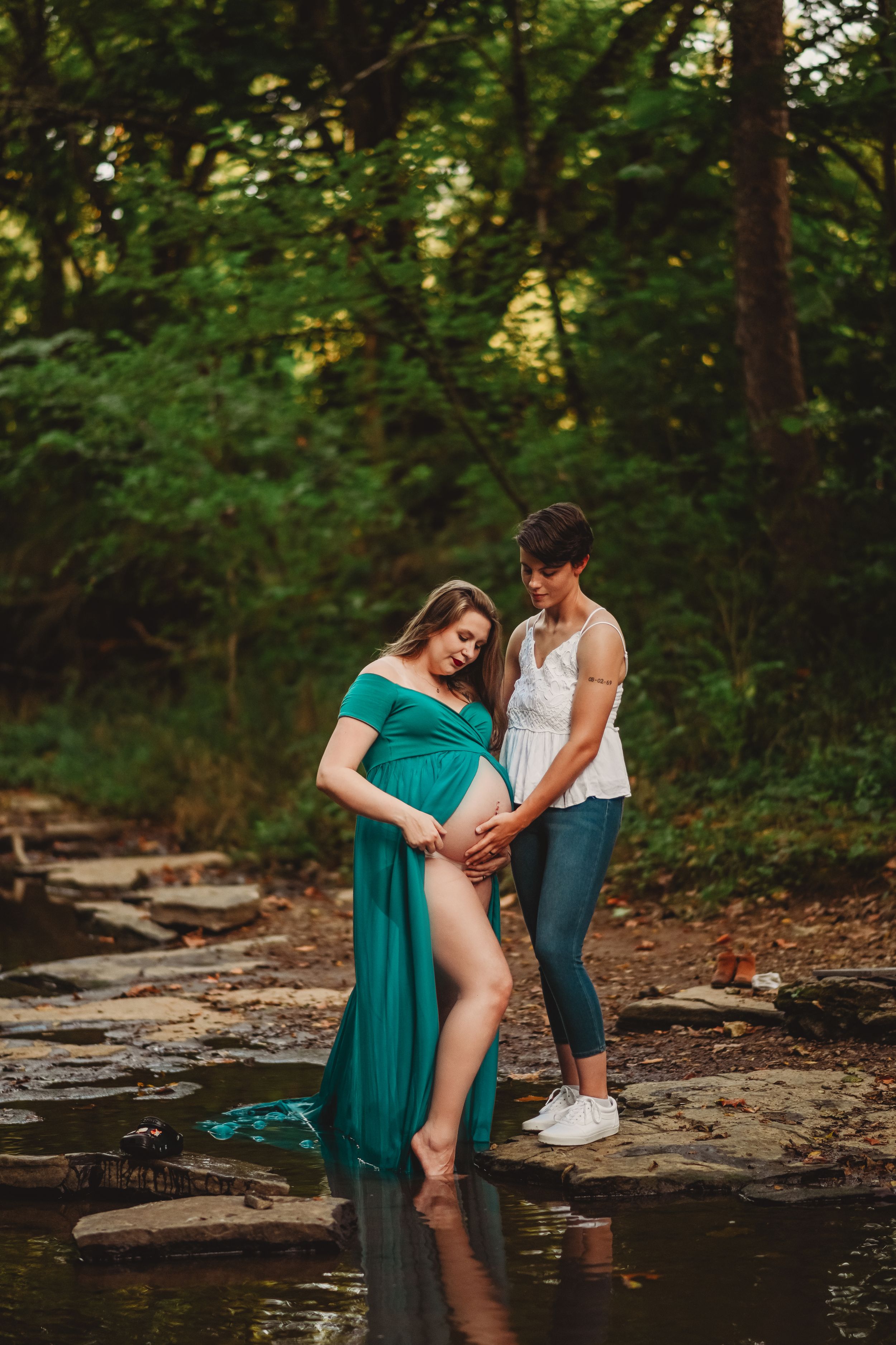 A romantic scene unfolds by a creek with a flowing teal dress against natural rocks.