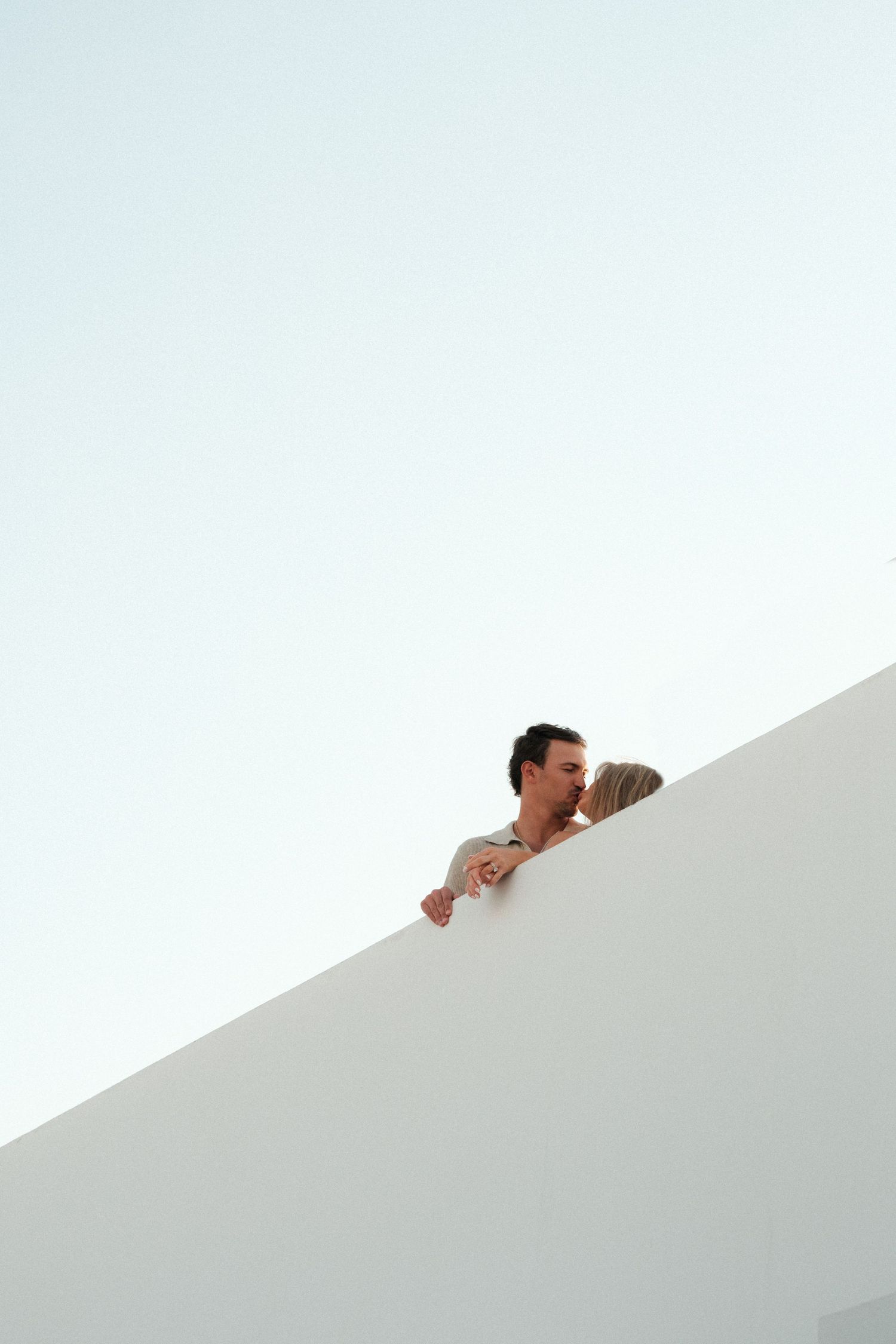 Couple embracing on a minimalist white rooftop against clear blue sky.